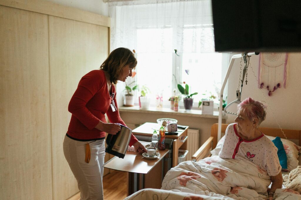 Caregiver Serving Tea to Old Woman in Retirement House